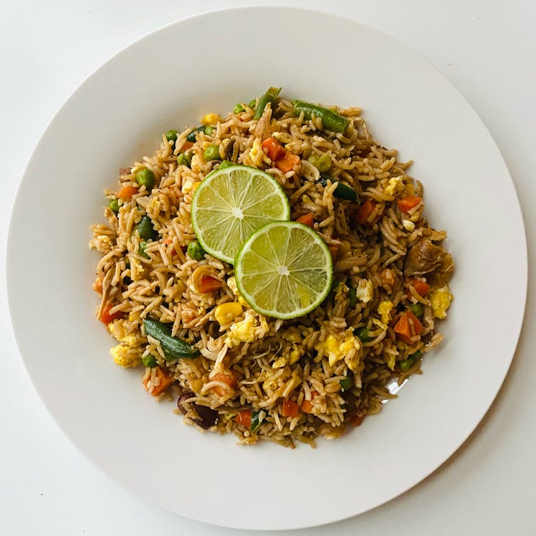 A delicious plate of vegetable fried rice topped with fresh lime slices.