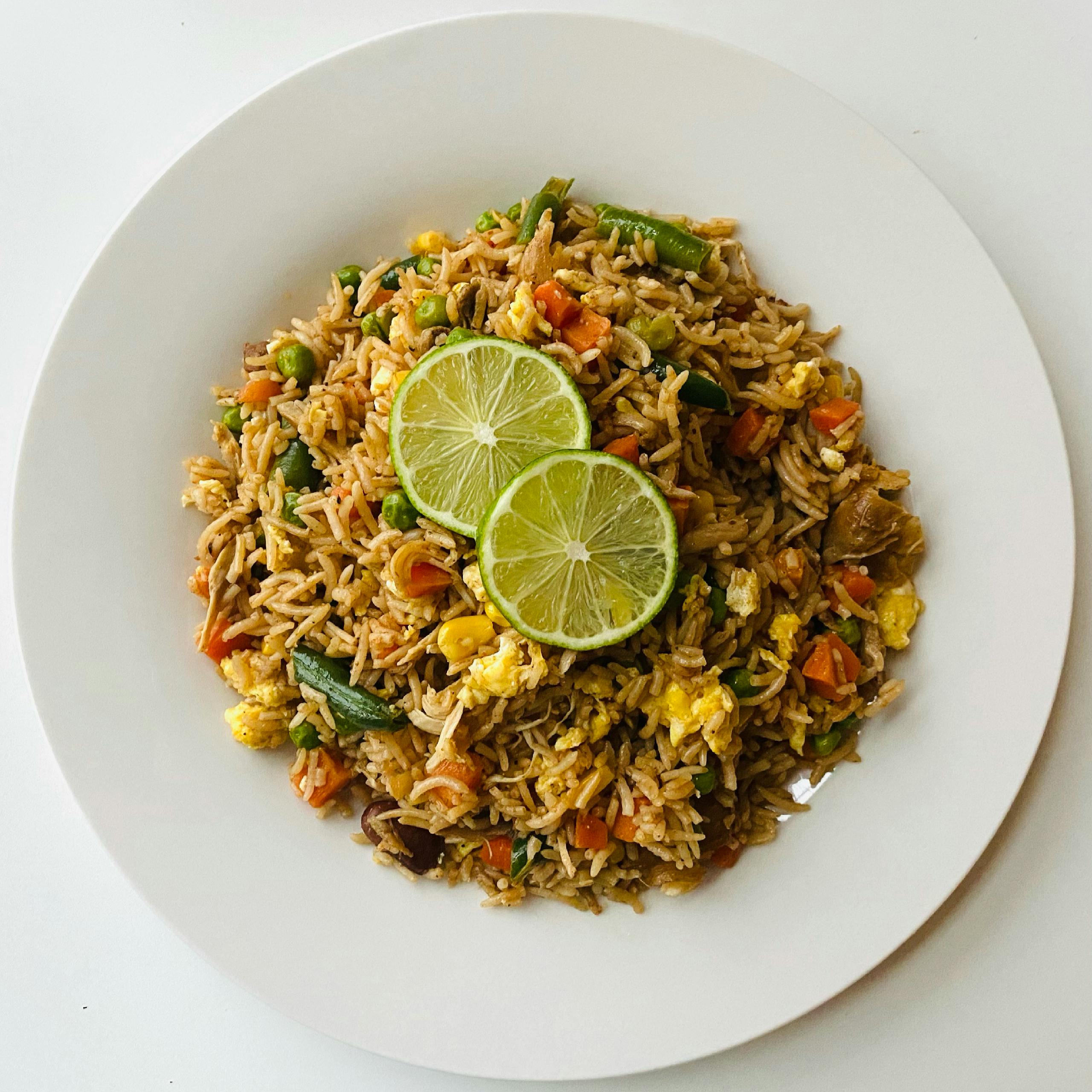 A delicious plate of vegetable fried rice topped with fresh lime slices.