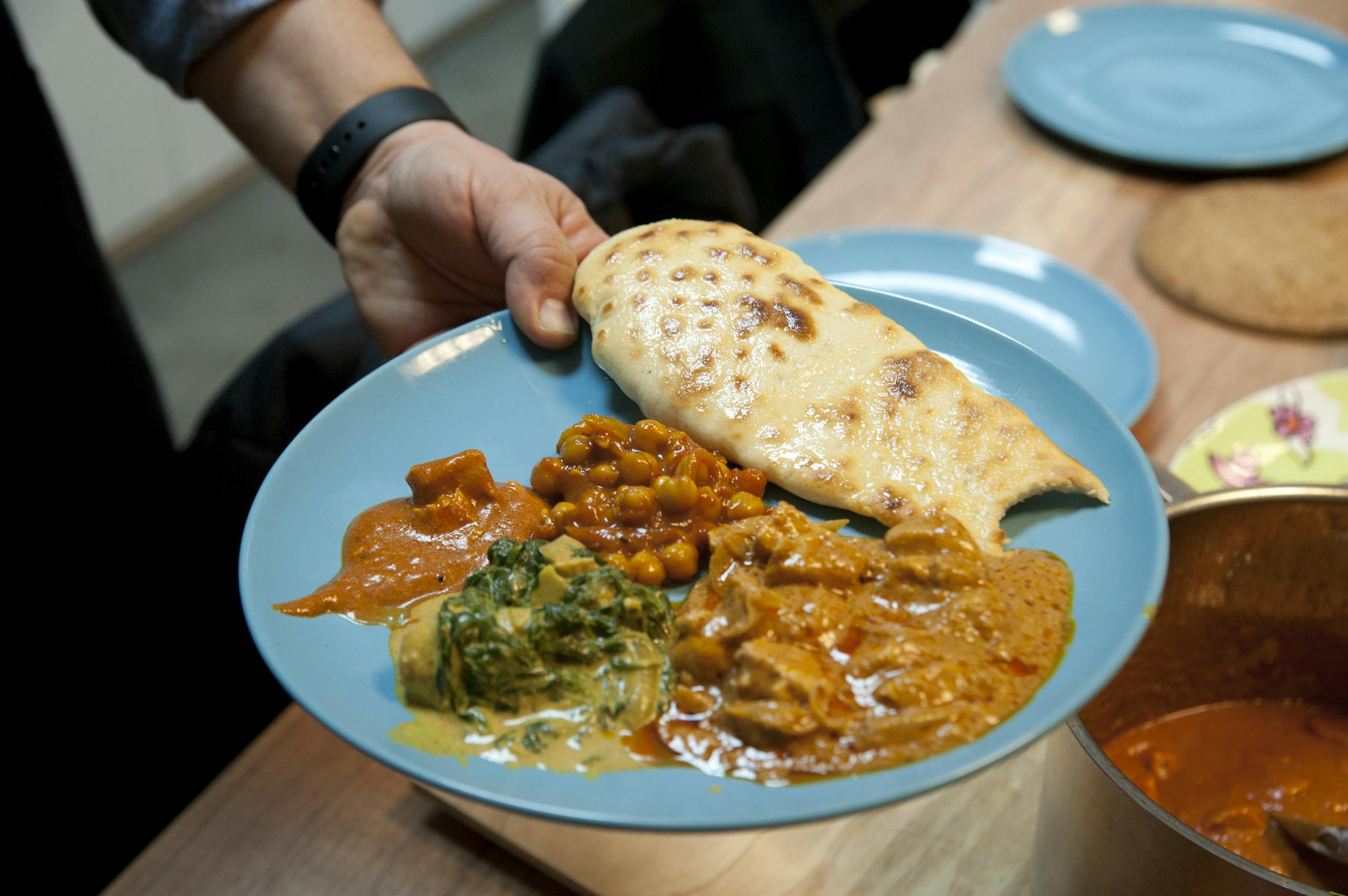 A vibrant blue plate featuring a variety of Indian curries and naan bread, served indoors.