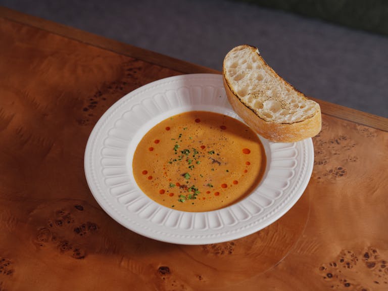 A warm bowl of pumpkin soup garnished with herbs and served with a slice of crusty bread.
