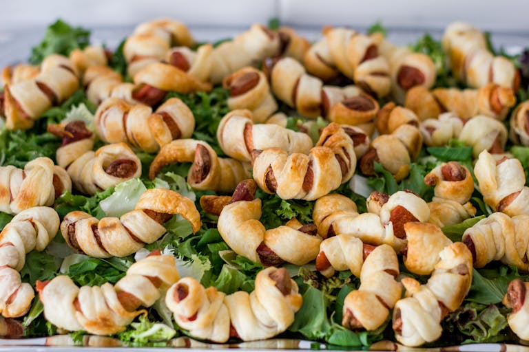 Baked puff pastry sausage rolls served on a bed of fresh leafy greens, perfect for parties.