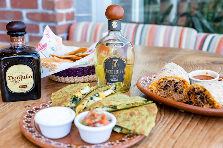 Close-up of a delicious Mexican meal with tequila, featuring burrito and quesadillas.