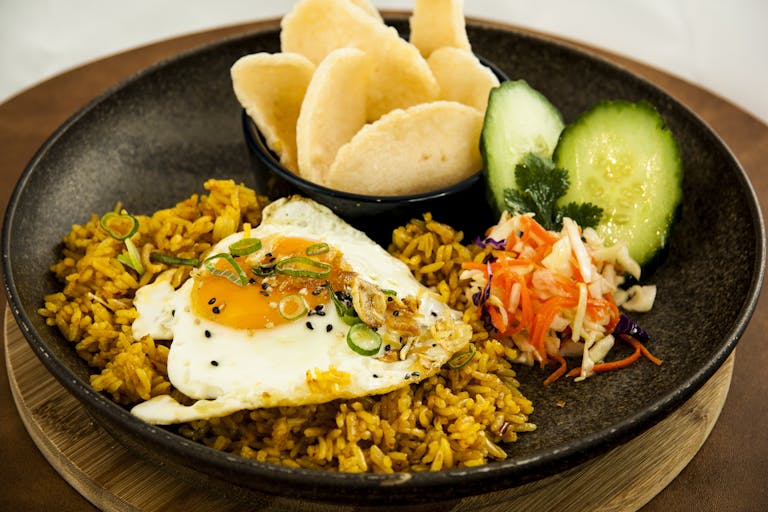Close-up of a plate with fried rice, egg, and fresh vegetables garnished with sesame seeds.