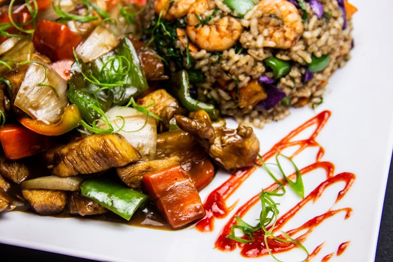 Colorful Brazilian stir fry with shrimp, chicken, and vegetables served on a white plate with sauce garnish.