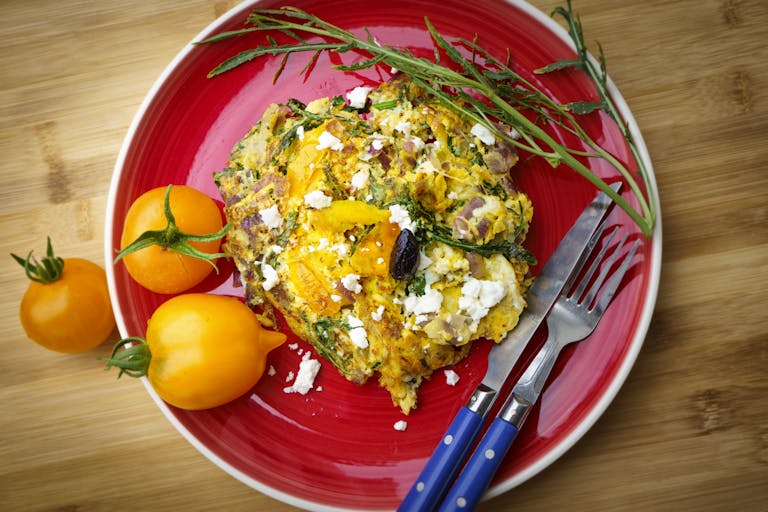 Delicious Greek frittata with tomatoes and feta on a vibrant red plate.