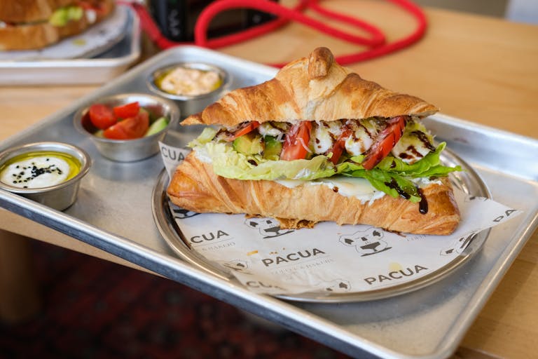 Tasty croissant sandwich filled with vegetables and sauces on a cafe tray.